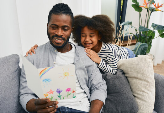 Father's Day. African American daughter gives daddy a greeting card which she drew herself and hugs him at home