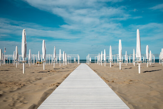Riviera Romagnola spring view. Almost summer, clue skies, white walking path, sunbeds and umbrellas ready for season opening. Italian vintage riviera beach on the adriatic coast. 