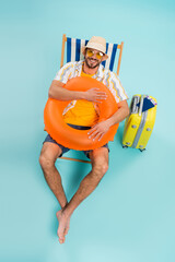 High angle view of happy man holding inflatable ring near suitcase and passports on blue background