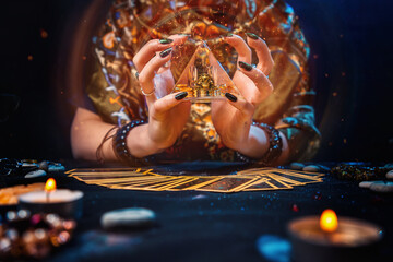 Sorcery. The witch held a glowing pyramid in her hands and conjured it. The tarot cards were on the table. Hands close-up. The concept of divination and astrology