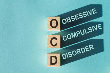 Wooden cubes building word OCD - (abbreviation Obsessive Compulsive Disorder) on light blue background.