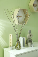 Glass vase with pussy willow tree branches and decor on white table near light green wall indoors