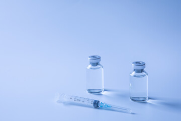 vials of medicine/vaccine and syringe against blue background
