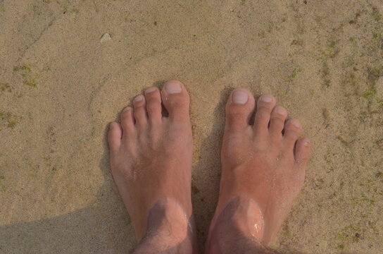 male feet step on the sand on the beach in summer