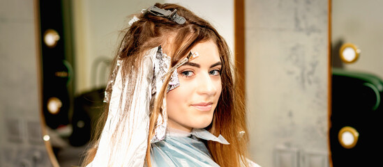 Fototapeta na wymiar Portrait of a beautiful young caucasian woman getting foil on her hair before dyeing in a beauty salon