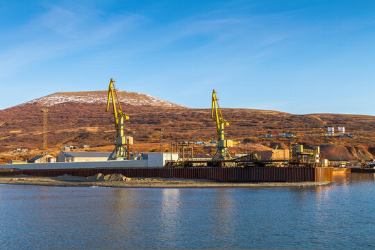 Cargo seaport in the North-East of Russia. View from the sea to the port cranes against the background of the hills. Northern port in the Arctic. Beringovsky, Chukotka, Siberia, Russia. Bering Sea.
