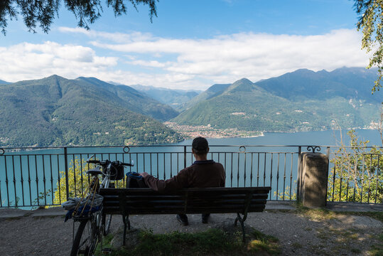 Big italian lake seen from above. Lake Maggiore, Italy with the city of Cannobio in the center and a tourist with a bicycle sitting on a bench. Vacation and tourism concept