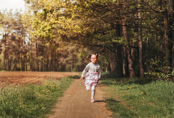 A little happy girl runs along a forest path in the summer on a sunny day