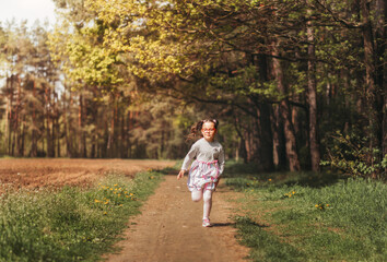 Fototapeta premium A little happy girl runs along a forest path in the summer on a sunny day