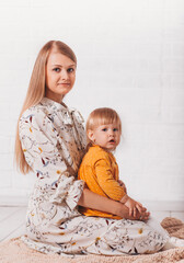 Young beautiful blonde woman is holding a little daughter on her lap. Vertical