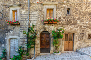 Fototapeta na wymiar Pescocostanzo, Italy. August 24th, 2012. Facades of historic buildings with entrance and windows decorated with plants and flower pots of different colors.