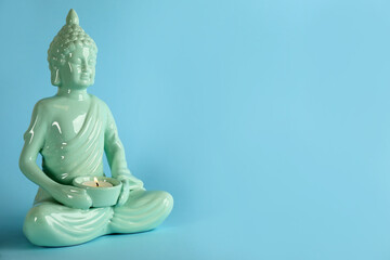 Beautiful ceramic Buddha sculpture with burning candle on light blue background. Space for text