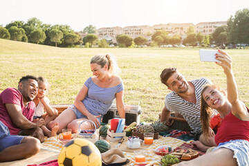 Happy multiracial families having fun doing selfie at picnic party outdoor in city park - Main focus on center woman face