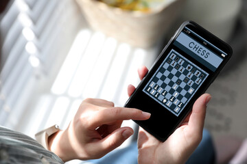 Woman playing online chess on smartphone indoors, closeup