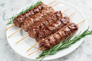 grilled Lula kebab on skewers with spices on a white plate on a light stone background