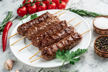 grilled Lula kebab on skewers with spices on a white plate on a light stone background