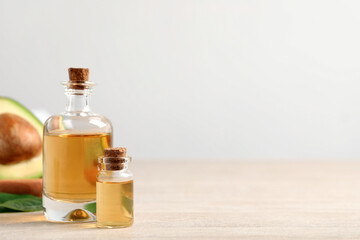 Bottles of essential oil and fresh avocado on light wooden table, space for text