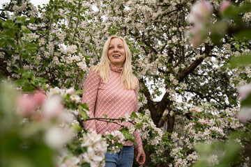 Blonde woman standing and posing in apple blossoms with dental braces, pink color