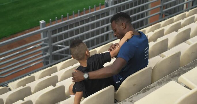 Diverse father and son hugging and watching match on stadium