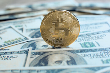 Bitcoin cryptocurrency coin stands on its own end on one hundred dollar bills