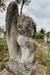 Close up view of broken weathered tombstone with stone angel on old abandoned city or village cemetery. Weathered gravestone on abandoned graveyard. Selective focus, sacral art details