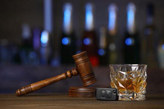Car key, glass of alcoholic drink and gavel on wooden table in bar, space for text. Drunk driving concept