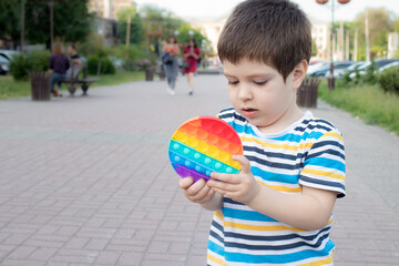 Fototapeta premium A child of 4 years plays with Pop It in the city park. Anti-stress toy for the development of fine motor skills in children.