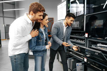 Male shop assistant helps young couple to choose new home appliance