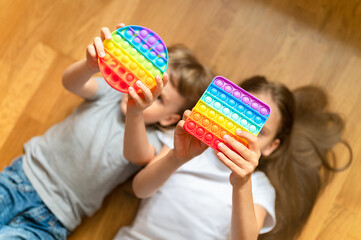 anti stress sensory pop it toys in a children's hands. a little happy kids plays with a simple dimple toy at home. toddlers holding and playing popit rainbow hue bright color, trend 2021 year - obrazy, fototapety, plakaty