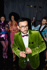 serious arab man dancing with interracial friends in colorful clothes near grey curtain on black background.