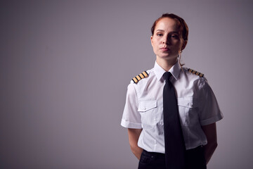 Studio Portrait Of Serious Young Female Airline Pilot Against Plain Background