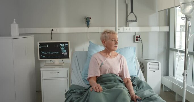 Ill mature woman with nasal cannula sitting in hospital bed