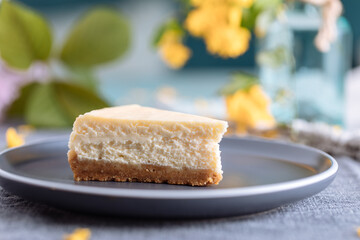Piece of New York cheesecake served on a grey plate with flower decoration