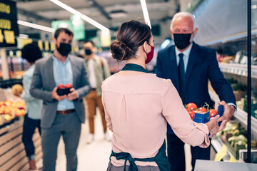 Grocery store employee is helping customers. They are all wearing face protective masks due to Coronavirus epidemic.