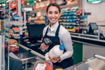 Portrait of beautiful smiling cashier working at a grocery store. - obrazy, fototapety, plakaty