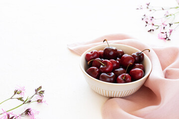 Cherries in a bowl on a pink napkin and with wildflowers on a white background