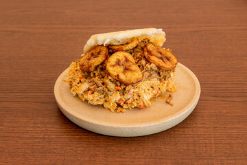 Colombian arepa with chicken meat and fried plantain slices on a round plate