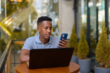 African businessman sitting at coffee shop while using laptop computer and mobile phone