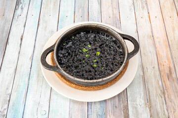metal casserole containing a portion of black seafood paella to serve as tapas in a Spanish restaurant