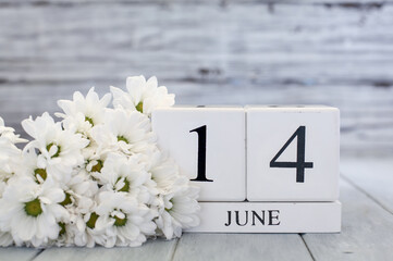 White wood calendar blocks with the date June 14th and white daisies. Selective focus with blurred background.