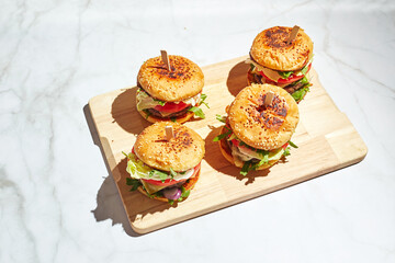 Appetizing homemade burgers on wooden cutting board with bright sunlight. Burger with veal cutlets, pamidorom, cheese, red onion, lettuce, rocket salad and french fries. Fast food concept