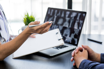 Close up of doctor  and patient taking, doctor working with laptop computer and writing on paperwork. Hospital background.
