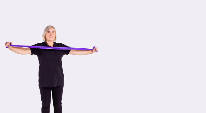 Everyday health for aged people. Sporty senior woman in black sportswear holding rubber resistance band while going to exercise at home. Workout, body goals concept on studio grey background for ad