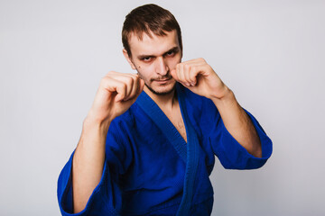 Young man in a blue kimono on a white background. The guy is new to martial arts.