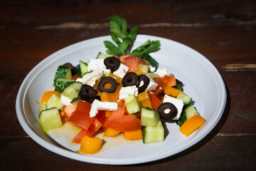 Fresh Greek salad in a disposable dish on a wooden table.