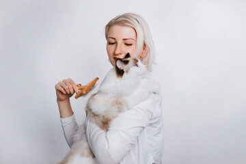 A girl in a white coat is holding a fluffy cat regg dol. Veterenar is combing the animal.