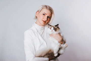 A girl in a white coat is holding a fluffy cat regg dol. Veterenar is combing the animal.