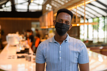 Fototapeta na wymiar African businessman wearing face mask in coffee shop restaurant