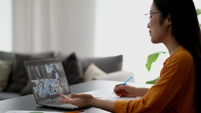 Video call, online conference, distant learning. Smart asian female student or freelancer, studies or works remotely, watches an online lecture, takes notes, multiracial people on laptop screen