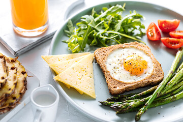 Sunny side up egg in a toast served with cheese, asparagus, rocket and tomatoes on a rustic white background